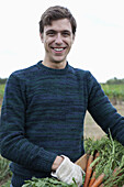 Man holding harvested carrots in field, portrait