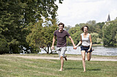 Young couple holding hands and running in park