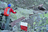 Frau wandert durch Blockfeld mit Felsen mit Markierung und Steinmann im Vordergrund, Trans-Lagorai, Lagorai-Höhenweg, Lagorai, Dolomiten, UNESCO Welterbe Dolomiten, Trentino, Italien