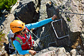 Woman ascending iron cramps on fixed rope route, fixed rope route Henne, Henne, Kitzbuehel range, Tyrol, Austria