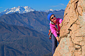 Woman climbing on red Granite rock with view to Monte Rosa in Valais, Mottarone, Piedmont, Italy