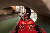 tourist trip on gondola in a narrow canal in historic Castello, art of rowing, gondolier, below bridge in narrow canal romantic, blurred, moving, Venice, Veneto, Italy