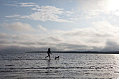 Girl Running With Shih-Bi Through Waters Of Lake Huron At Singing Sands Beach, Bruce Peninsula National Park, South Of Tobermory, Ontario