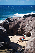 'Woman reading in a secluded piece of beach at Ho'okipa Beach Park; Paia, Maui, Hawaii, United States of America'