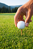 'Golfer sets up a ball on the tee of a golf course on a summer evening; Whistler, British Columbia, Canada'