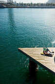 'A couple laying on a wooden dock at the water's edge in the warm sunshine; Barcelona, Spain'