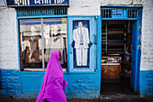'Veiled woman in pink walks past a tailors shop in the old city of Harar in Eastern Ethiopia; Harar, Ethiopia'