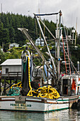 Fishing boat with small shoreside cottages and trees in the backgroud at the Cordova small boat harbor, Prince William Sound, Southcentral Alaska, USA.