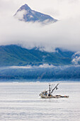 Commercial fishing boat Silver salmon fishing outside of Valdez small boat harbor with misty clouds and mountains in background, Prince William Sound, Southcentral Alaska, USA.