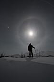 'Man snowshoeing along the Dempster Highway under a moon glowing with rings; Yukon, Canada'
