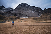 Mountain peak rises above female hiker hiking trail towards Horseid beach, Moskenes??y, Lofoten Islands, Norway