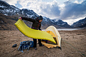 Female hiker sets up tent on wild camping trip to Horseid beach, Moskenes??y, Lofoten Islands, Norway