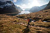 Female hiker descending trail to catch ferry at village of Kjerkfjord, Moskenes??y, Lofoten Islands, Norway