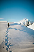 A snowshoer walks a snow covered ridgeline with Mount Baker in the background.