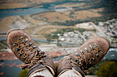 A hiker dangles their boots over the edge of the Chief Mountain in Squmish, BC, Canada.