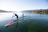 A fit male and female paddle their stand up paddle boards (SUP) at sunset on Whitefish Lake in Whitefish, Montana.