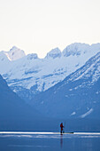 A man stand up paddle boards (SUP) on a calm Lake McDonald at sunrise in Glacier National Park near West Glacier, Montana.