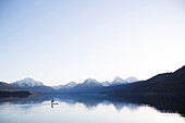 A man stand up paddle boards (SUP) on a calm Lake McDonald at sunrise in Glacier National Park near West Glacier, Montana.