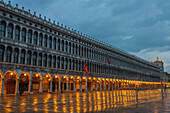 'Lighted archways in a row along a building reflected in the wet pavement, Piazza san marco; Venice, Veneto, Italy'