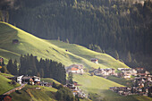 'Sun lit rolling grassing slopes with alpine houses and barns; Lanserbach, Austria'
