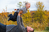 'Father holding his son high in the air pretending to fly; Edmonton, Alberta, Canada'
