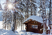 'View of a public use log cabin at Byers Lake in fresh snow under a sun burst, Interior Alaska; Alaska, United States of America'