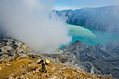 Worker loaded with big pieces of sulphur in front of steam clouds on the Ijen crater lake, Java, Indonesia, Southeast Asia, Asia