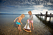 Two girls with a toy sailboat in lake Starnberg, Upper Bavaria, Bavaria, Germany