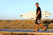 Side view of man walking along ocean carrying surf board