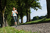 Young woman jogging, alley near Aufkirchen, Berg, Bavaria, Germany