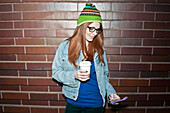 Junge Frau mit Kaffee zum Mitnehmen und Blick auf ihr Smartphone