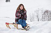 Junge Frau sitzt auf einem Schlitten, Spitzingsee, Oberbayern, Bayern, Deutschland