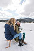 Zwei junge Frauen sitzen auf einem Schlitten, Spitzingsee, Oberbayern, Bayern, Deutschland