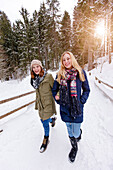Two young women arm in arm walking in snow, Spitzingsee, Upper Bavaria, Germany