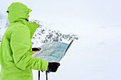 Frau auf Skitour blickt bei Schlechtwetter auf Landkarte, Serriera di Pignal, Valle Stura, Cottische Alpen, Piemont, Italien