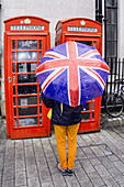 Frau mit Regenschirm vor ropten Telefonzellen, London, UK