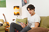 Young man sitting on the sofa and playing on the tablet
