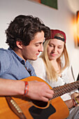Young couple relaxing on the sofa, playing the guitar