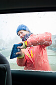 Young woman de-icing the car's window, Cuxhaven, North Sea, Lower Saxony, Germany