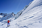 Woman back-country skiing ascending towards Punta San Matteo, Punta Cadini and icefall in background, Punta San Matteo, Val dei Forni, Ortler range, Lombardy, Italy