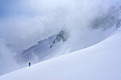 Frau auf Skitour steigt durch Wolkentreiben zum Grundschartner auf, Grundschartner, Zillergrund, Zillertaler Alpen, Tirol, Österreich
