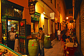 Schmale Gasse mit Tischen und Restaurant mit Meeresfrüchten nahe der Kathedrale von von Malaga im Abendlicht, Malaga, Andalusien, Spanien