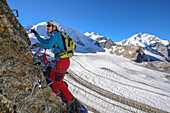 Woman climbing the via ferrata at Piz Trovat with view to Piz Palue (3905 m), Bellavista (3922 m), Piz Bernina (4049 m), and Pers glacier, Engadin, Grisons, Switzerland