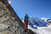 Woman climbing the via ferrata at Piz Trovat with view to Piz Palue (3905 m), Bellavista (3922 m) and Pers glacier, Engadin, Grisons, Switzerland