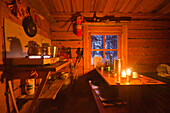 Ein Tisch mit Kerzen, Tassen und Thermosflaschen und Töpfe auf dem Gasherd bei Kerzenlicht, Kuusela Hütte, Urho Kekkonen Nationalpark, finnisch Lappland, Finnland