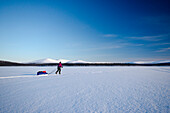 Eine Frau auf Ski zieht eine Pulka über den gefrorenen See namens Luirojärvi, Urho Kekkonen Nationalpark, finnisch Lappland, Finnland