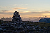 A cairn on the mountain called Silberen in the early morning, in the background in the middle the silhouette of the summits of Churfirsten, on the right the three summits of Muertschenstock, Glarus Alps, cantons of Schwyz, Glarus and St. Gall, Switzerland