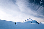 An alpine hiker walking across the glacier named Glatscher da Medel, in the background Piz Medel, Grison Alps, Switzerland