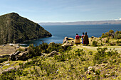 Three cholitas, native women in traditional clothing, on a path on the island of Isla del Sol, in the background Lake Titicaca, Bolivia