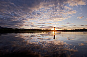 Frau beim Stand Up Paddling auf dem Chiemsee im Sonnenuntergang, Chiemgau, Bayern, Deutschland